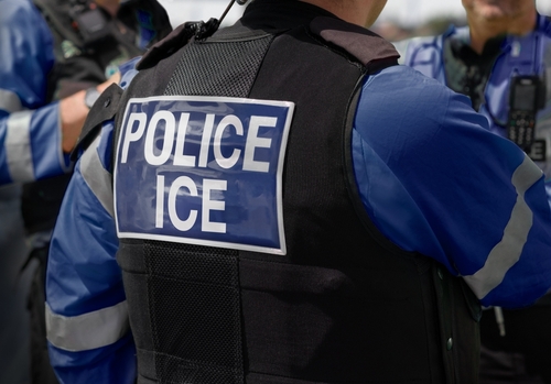 ICE police agent - Officer of Immigration and Customs Enforcement. Close-up of POLICE ICE marking on the back of a stab proof vest uniform worn by a trio of police officers at the scene of an immigrant incident. The ICE federal law enforcement agency is un