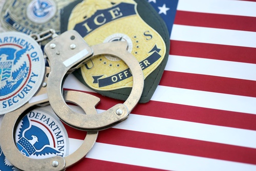 KYIV, UKRAINE - OCTOBER 31, 2025 US Immigration and Customs Enforcement ICE agent badges and handcuffs on table with United States flag background close up